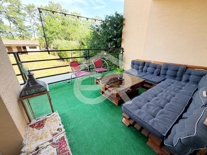 Balkon eines Einfamilienhauses mit Palettensitzmöbeln, grünem Teppich und Blick auf den Garten.