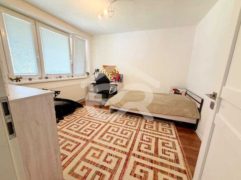 Ein Zimmer in einem Einfamilienhaus mit Teppichmuster und einem Boden in Holzoptik.