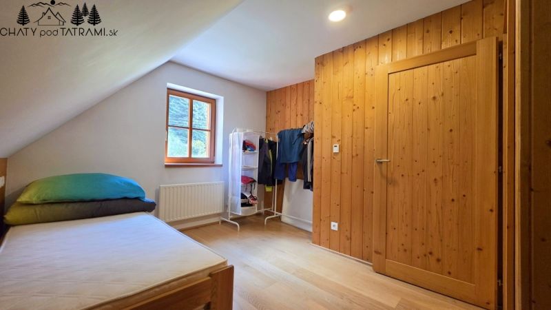 Ein Teil des Schlafzimmers in der Hütte mit einem Bett, einem Fenster und einem Kleiderhaken, Boden mit Holzdekor.