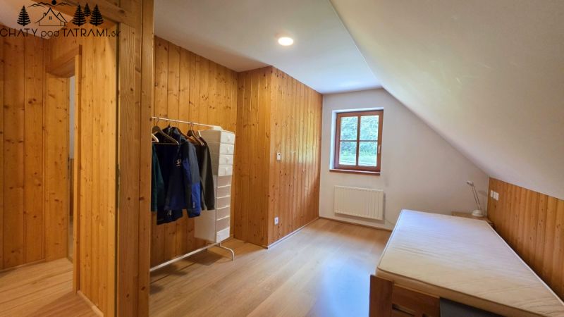 Ein Zimmer mit Holzvertäfelung und einem Boden in Holzoptik, einem Bett und einem Fenster.