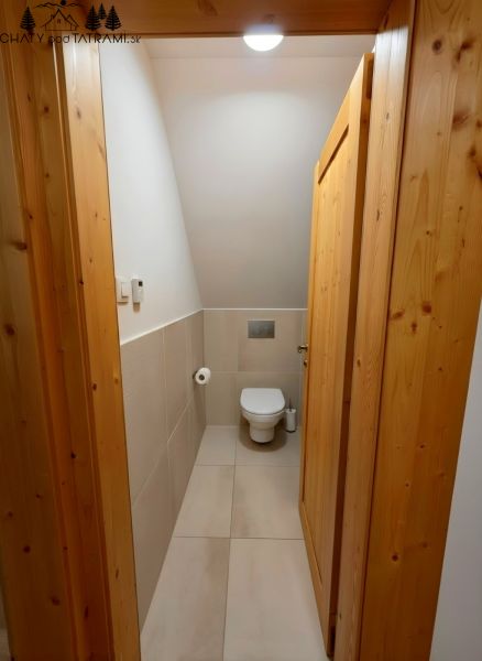 Innenraum der Hütte mit WC, helle Fliesen und Holzverkleidung der Wände und Türen.