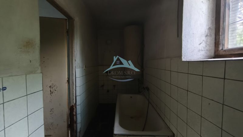 Ein Badezimmer mit Badewanne und Fliesen in einem Einfamilienhaus. An der Wand sind Schäden sichtbar.