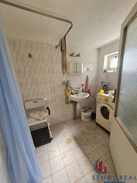 Badezimmer in einem Einfamilienhaus mit Waschmaschine, Duschkabine und kleinem Fenster.