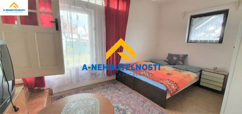 Ein Zimmer mit einem Bett, einem Fenster mit roten Vorhängen und einem Fernseher in einem Einfamilienhaus.
