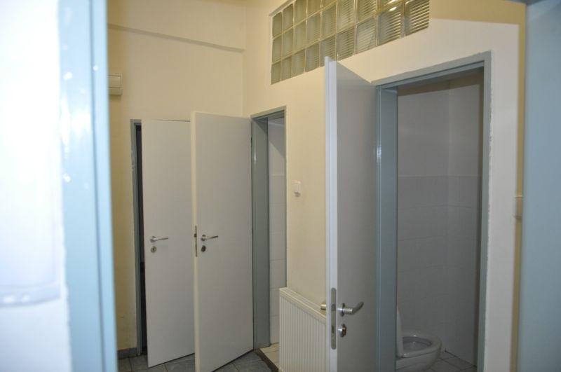 Offene Toilettentür in Produktionsräumen mit Fliesenboden und Waschbecken.