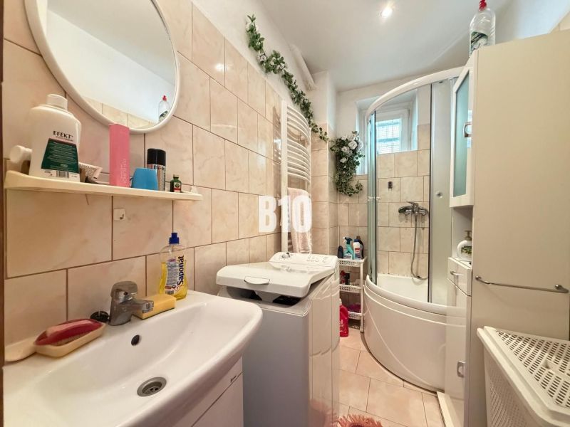 Badezimmer in einem Einfamilienhaus mit Waschmaschine, Badewanne, Waschbecken und Regal mit Produkten.