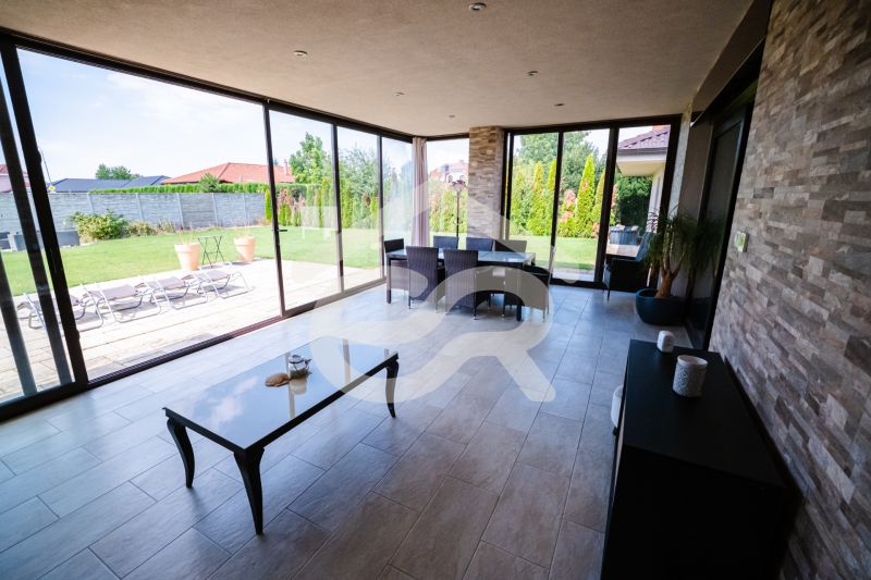 Ein verglaster Terrassenbereich eines Einfamilienhauses mit Blick auf den Garten und einem Boden aus Pflastersteinen.