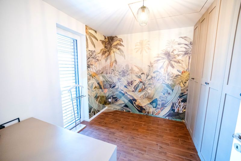 Ein Zimmer in einem Einfamilienhaus mit exotischer Tapete und Boden in Holzoptik.