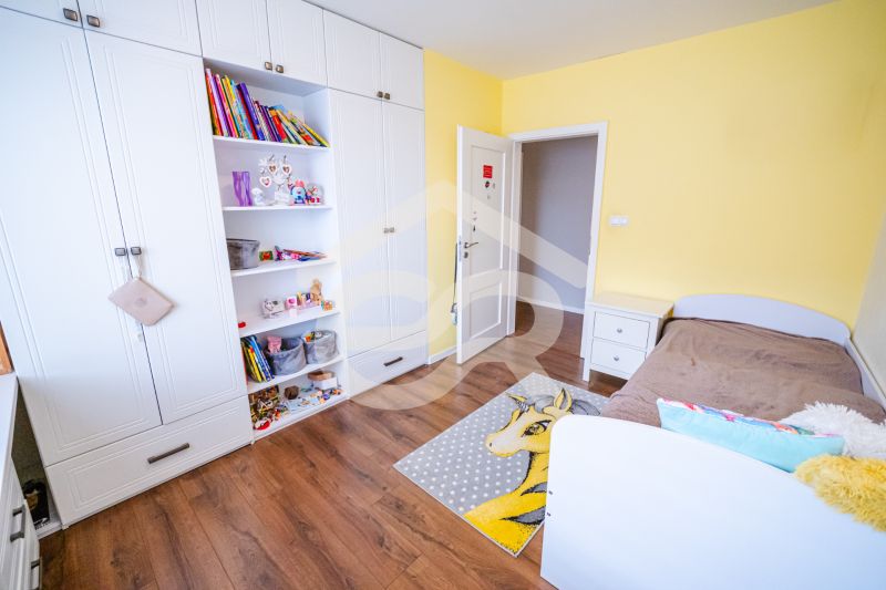 Kinderzimmer in einem Einfamilienhaus mit einem weißen Schrank, einem braunen Bett und einem Boden mit Holzdekor.