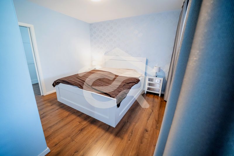 Schlafzimmer in einem Einfamilienhaus mit Bett, Nachttischen und Boden in Holzoptik.