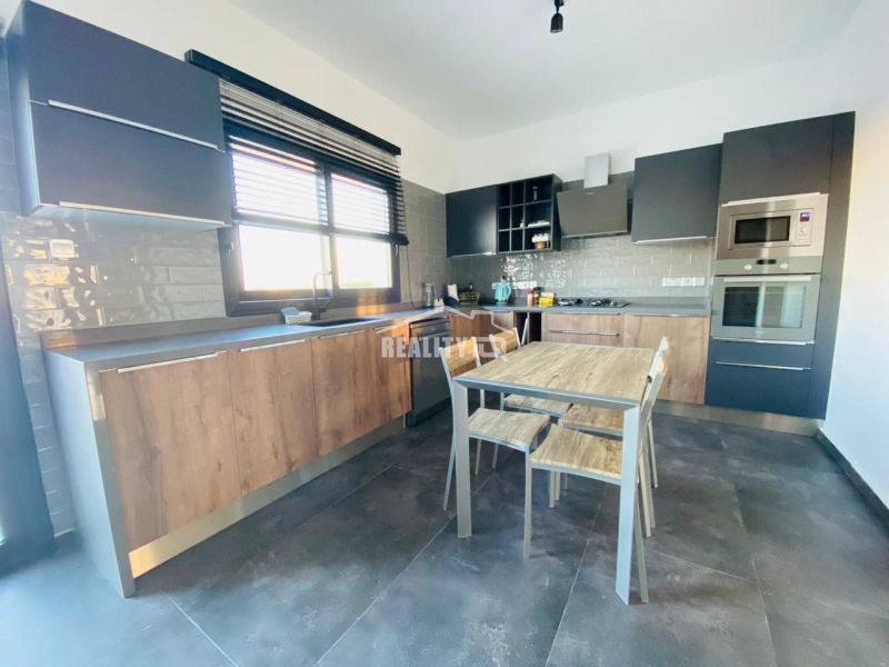 Küche mit Holzdekor, moderne Geräte, geräumiger Tisch und graue Schränke.