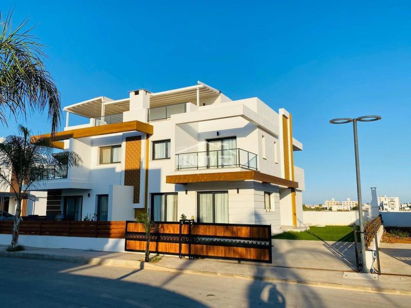 Ein Einfamilienhaus in Yeni Boğaziçi mit weißer Fassade, Holzelementen und Palmen auf dem Grundstück.