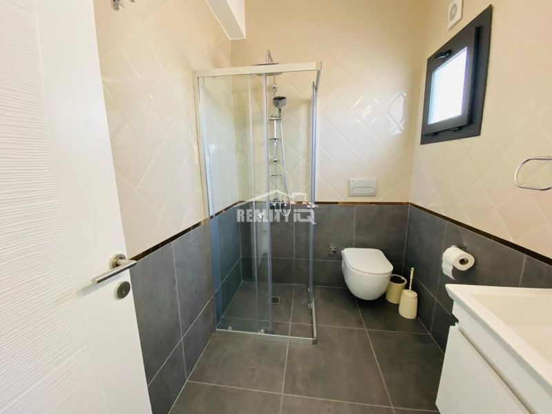 Ein Badezimmer in einem Einfamilienhaus mit Dusche, dunklen Fliesen und hellen Wandverkleidungen.