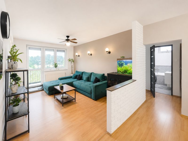 Wohnzimmer in einer 4-Zimmer-Wohnung mit einer türkisfarbenen Couch, einem Aquarium und einem Boden in Holzoptik.