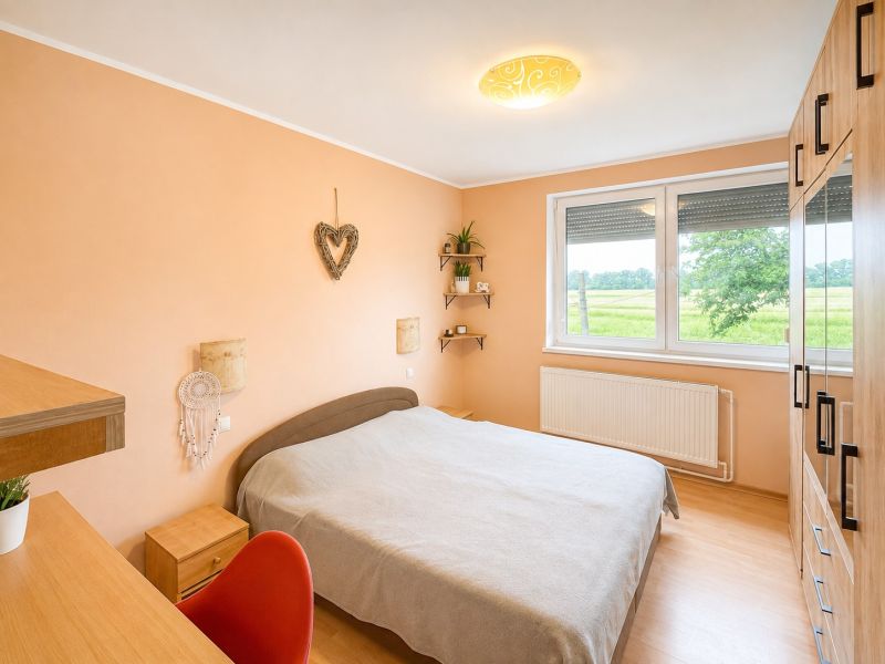 Schlafzimmer einer 4-Zimmer-Wohnung mit Holzboden, orangefarbenen Wänden und Blick ins Grüne.