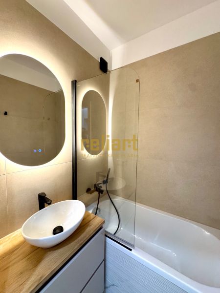 Badezimmer in einer 3-Zimmer-Wohnung mit Badewanne, Waschbecken auf Holzdekor und Spiegel.