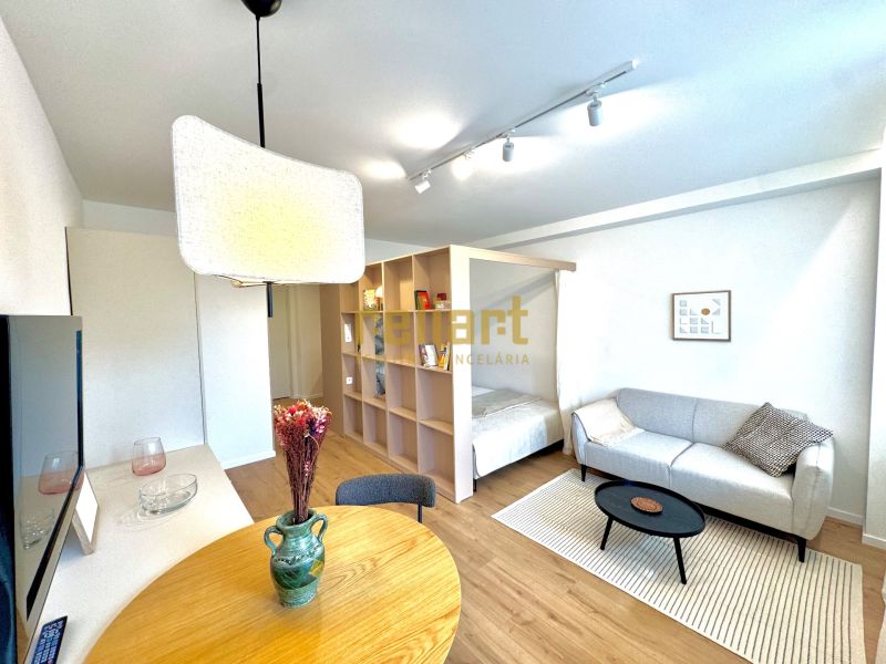 Wohnzimmer mit Holzboden, heller Couch und Esstisch in einer Einzimmerwohnung.