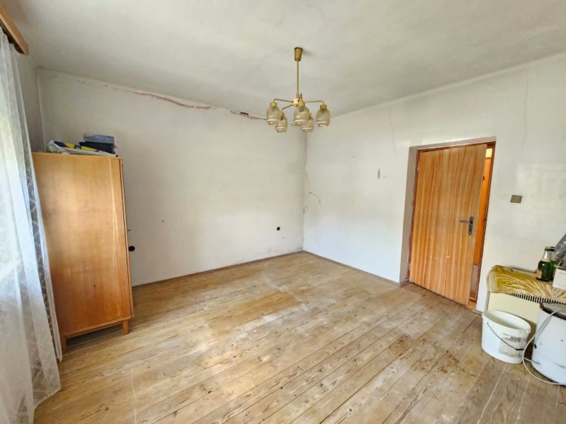 Ein Zimmer in einem Einfamilienhaus mit Holzboden, Kleiderhaken und einer einfachen Deckenlampe.