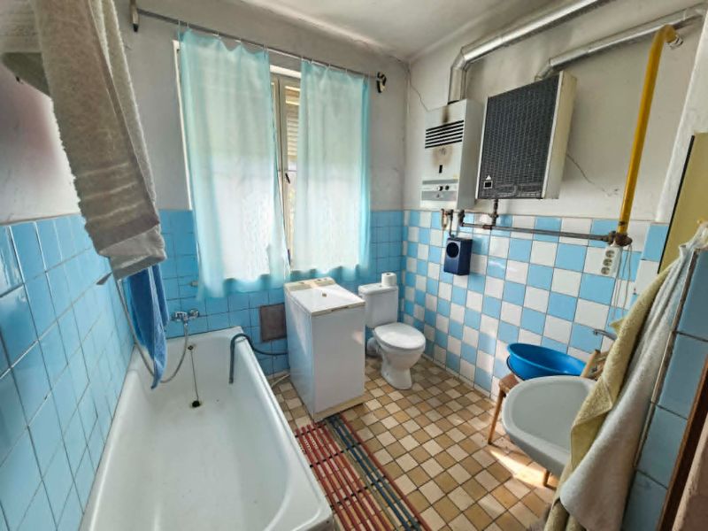 Ein Badezimmer in einem Einfamilienhaus mit älteren hellblauen Fliesen und einer Badewanne.