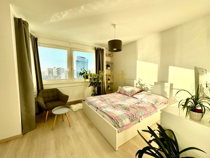 Helles Schlafzimmer mit Bett, Sessel und Holzboden in einer Einzimmerwohnung.