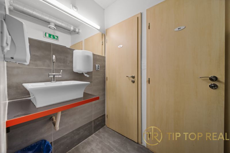 Badezimmer in Geschäftsräumen mit Waschbecken, zwei Holztüren und Fliesen.