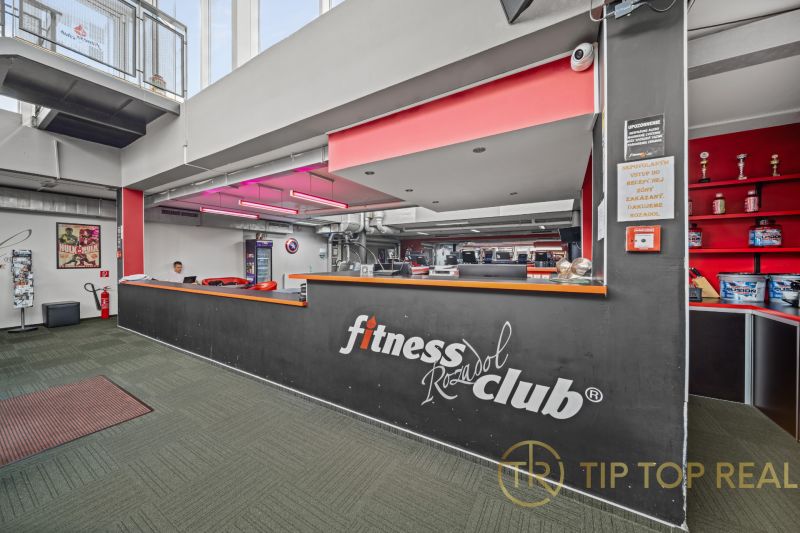 Rezeption eines Fitnessstudios mit einem Schild, roter Beleuchtung und dekorativen Trophäen auf einem grünen Boden.