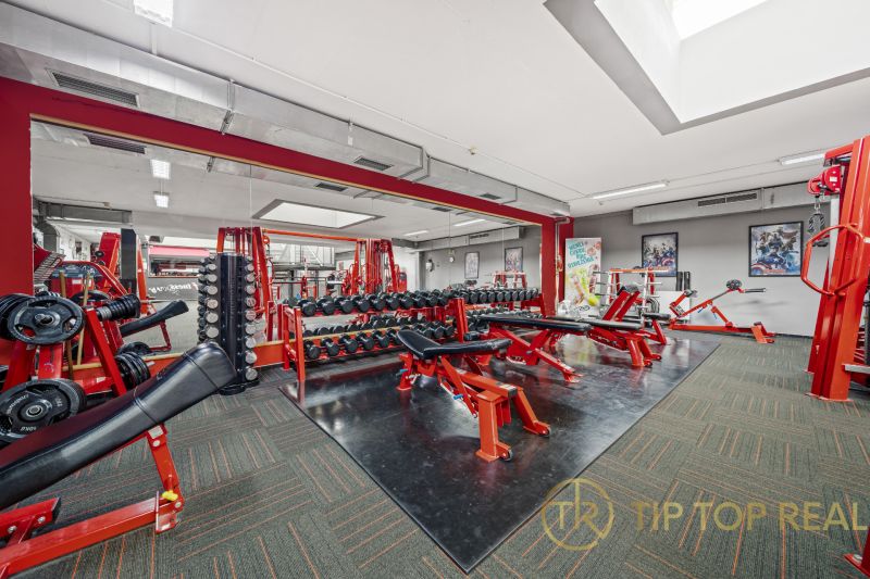 Fitnesscenter mit Kraftgeräten, Bänken und Spiegeln in Geschäftsräumen.
