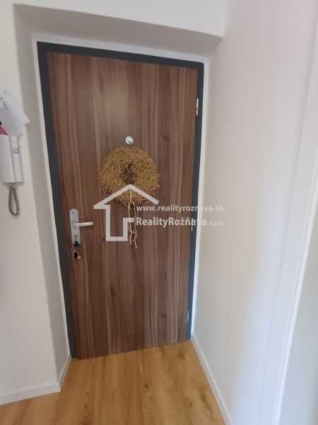 Eingangstür in einer 2-Zimmer-Wohnung mit einem Kranz und einem Boden in Holzoptik.