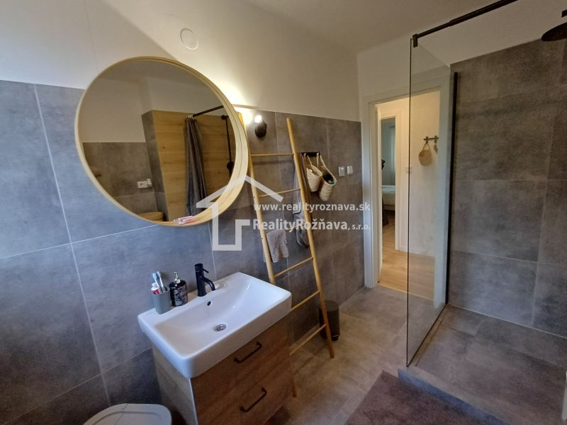 Badezimmer in einer 2-Zimmer-Wohnung mit Duschkabine, Waschbecken und rundem Spiegel.