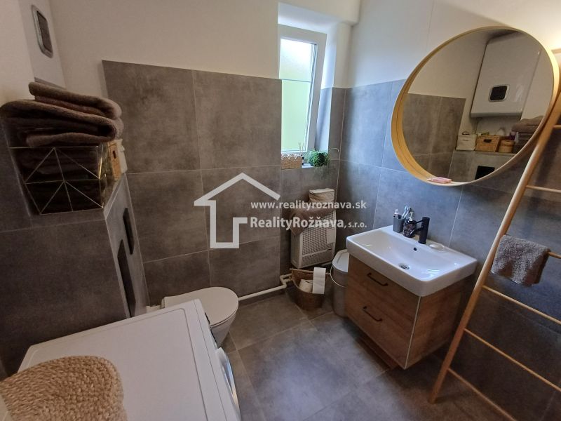 Badezimmer in einer 2-Zimmer-Wohnung mit rundem Spiegel und praktischem Stauraum.