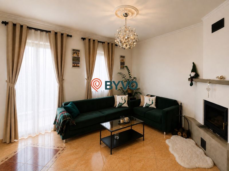 Wohnzimmer in einem Einfamilienhaus mit dunkelgrünem Sofa, Kamin und großen Fenstern.