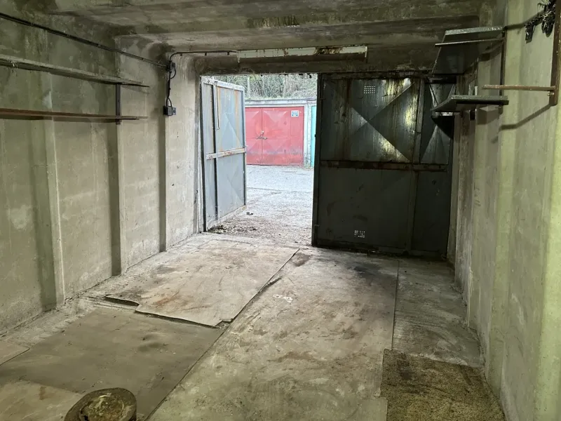 Betongarage mit offenen Stahltüren, Blick auf eine weitere Garage draußen.