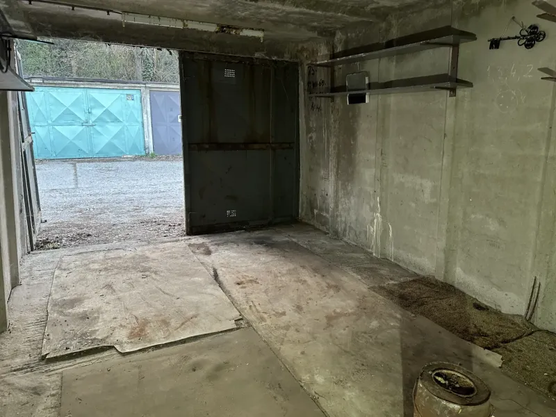 Innenraum einer Garage mit Betonboden und Metallregalen.