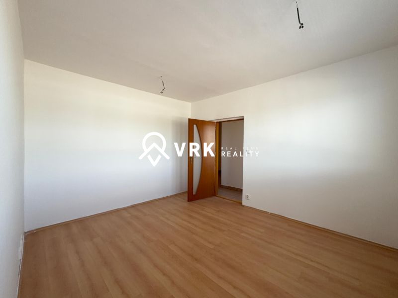 Ein Zimmer in einer 2-Zimmer-Wohnung mit einem Boden in Holzoptik und weißen Wänden.