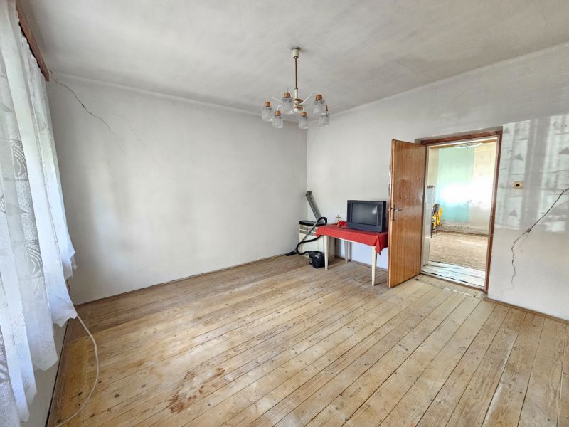 Ein Zimmer mit Holzboden in einem Einfamilienhaus, ein Tisch und ein älterer Fernseher.