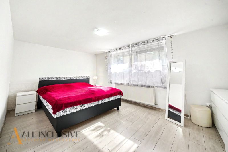 Schlafzimmer in einem Einfamilienhaus mit rotem Bett und Boden in Holzoptik.