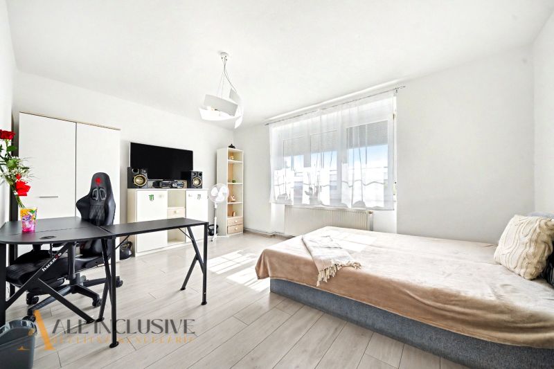 Helles Zimmer in einem Einfamilienhaus mit Bett, Tisch und Boden in Holzoptik.