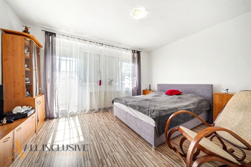 Ein Schlafzimmer in einem Einfamilienhaus mit einem Boden in Holzoptik, durchdacht angeordneten Möbeln und einem Schaukelstuhl.