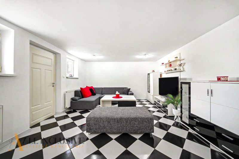 Wohnzimmer in einem Einfamilienhaus mit schwarz-weißem Schachbrettboden und grauem Sofa.