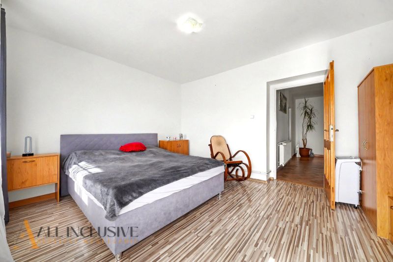 Ein Schlafzimmer in einem Einfamilienhaus mit einem bequemen Bett, einem Schaukelstuhl und einem Boden mit Holzdekor.