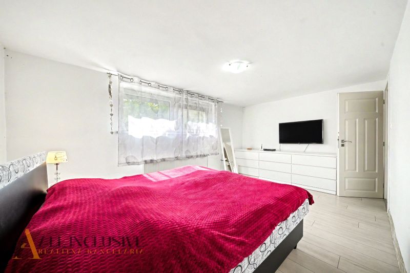 Helles Schlafzimmer mit roter Decke, Fernseher an der Wand und Holzboden.