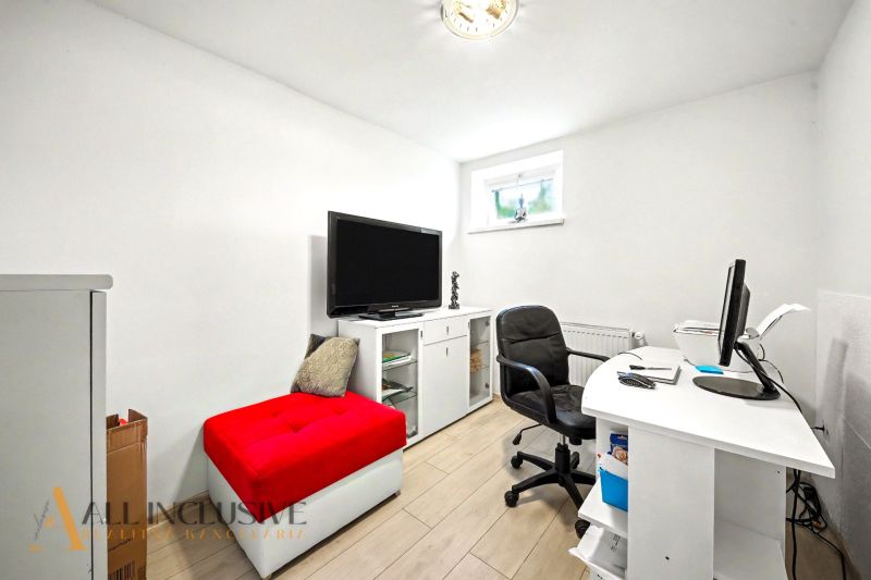 Ein Arbeitszimmer in einem Einfamilienhaus mit weißen Möbeln und einem roten Hocker.