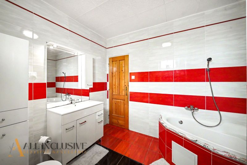 Das Badezimmer eines Einfamilienhauses mit roten und weißen Fliesen, einer Eckbadewanne und Schränken.