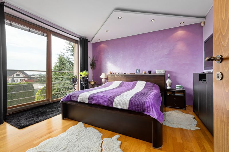 Ein Schlafzimmer in einem Einfamilienhaus mit einer lila Wand, einem Bett und einem Boden in Holzoptik.