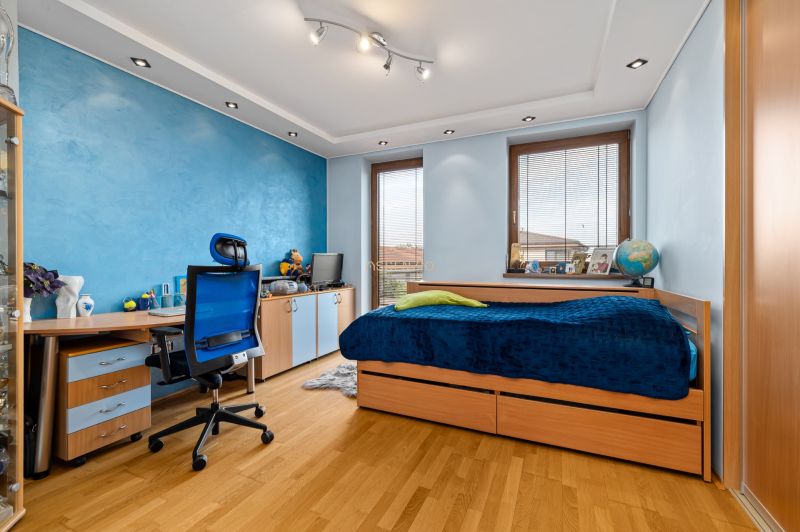 Kinderzimmer mit blauer Wand, Bett, Schreibtisch und Boden in Holzoptik.
