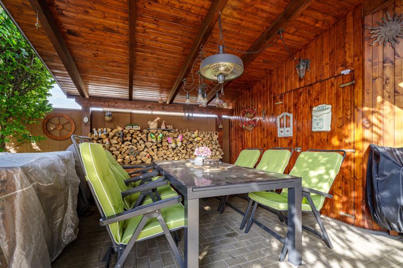 Ein Holzpavillon mit Steinboden und grünen Stühlen bei einem Einfamilienhaus.