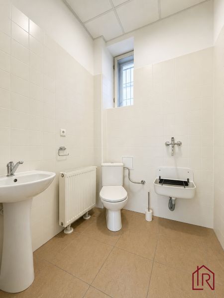 Toilette in Büros mit beigen Fliesen und Waschbecken.