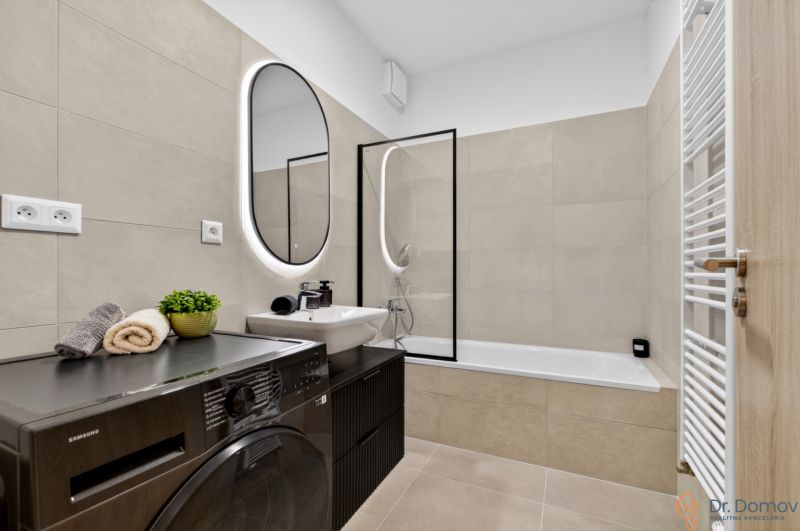 Badezimmer mit Badewanne, Waschmaschine und Spiegel in einer Zweizimmerwohnung.