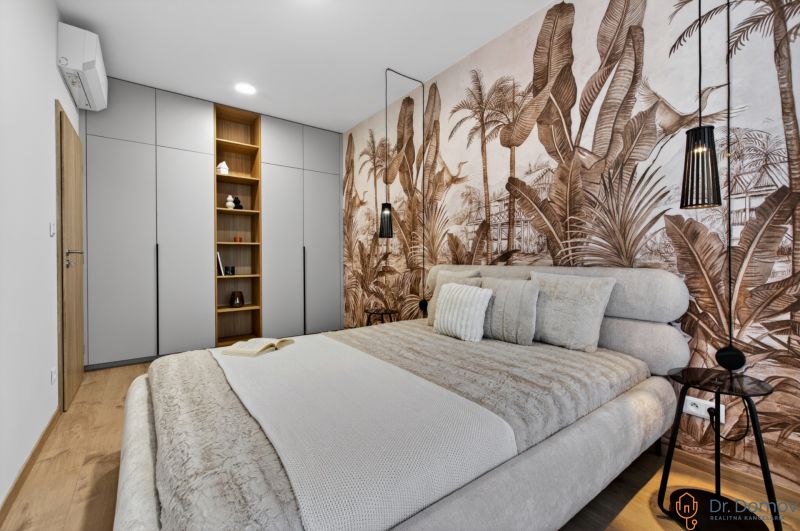 Schlafzimmer in einer 2-Zimmer-Wohnung mit Holzboden und Tapete mit exotischem Motiv.