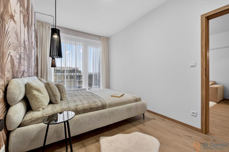 Schlafzimmer mit hellen Möbeln, Boden in Holzoptik, großem Fenster und Vorhang.